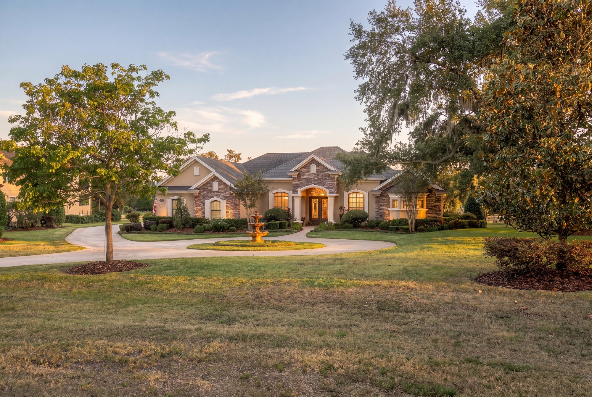 Stone and stucco home at golden hour with a circular drive and a tiered fountain