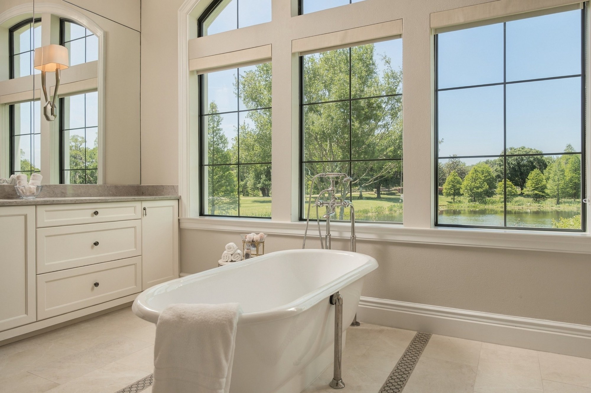Bathroom with a freestanding tub in front of tall windows overlooking a pond